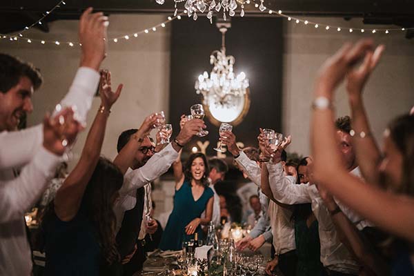 Invités souriants portant un toast avec des verres à champagne lors d'un dîner de mariage chaleureux et festif.