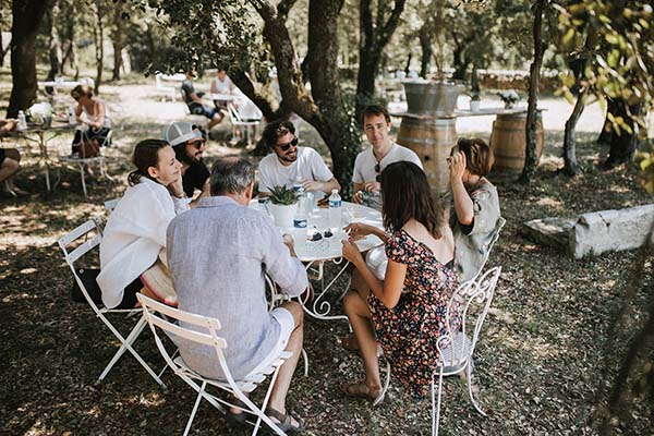 Des invités discutent joyeusement autour d'une table blanche dans un jardin ombragé lors d'un mariage décontracté.