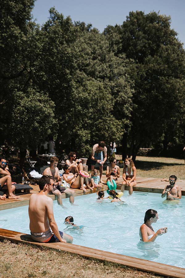 Invités se relaxant autour d'une piscine extérieure entourée d'arbres lors d'un mariage décontracté et ensoleillé.