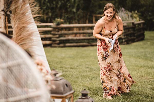 Une femme souriante en robe longue fleurie prononce un discours lors d'un mariage champêtre en plein air.
