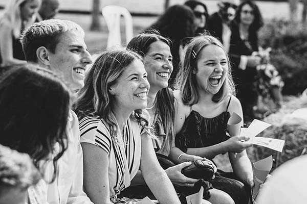 Groupe de jeunes femmes riant avec complicité lors d'un mariage champêtre, photographie en noir et blanc.