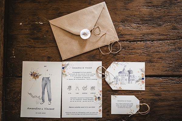 Papeterie de mariage champêtre beige et blanche avec illustrations minimalistes sur un fond de bois rustique.