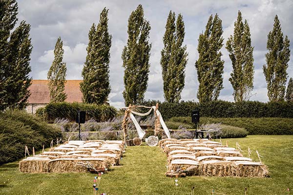 Cérémonie de mariage champêtre en plein air avec des bottes de paille et une arche bohème sous des peupliers.