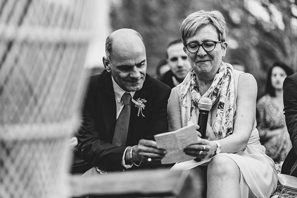 Photo noir et blanc d'un couple d'invités attentifs lisant un discours lors d'un mariage champêtre.
