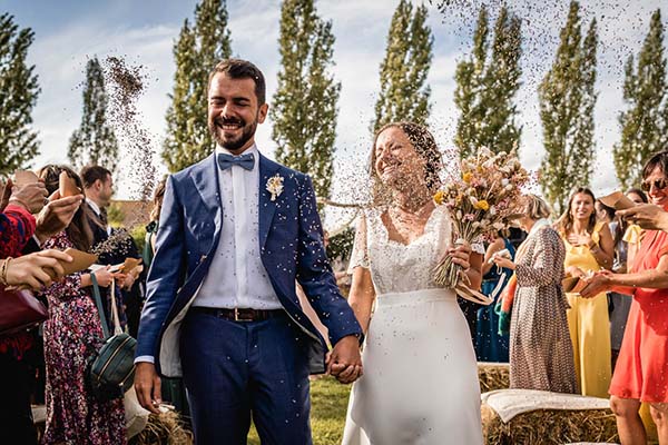 Jeunes mariés souriants sous une pluie de confettis lors d'une cérémonie champêtre en plein air.