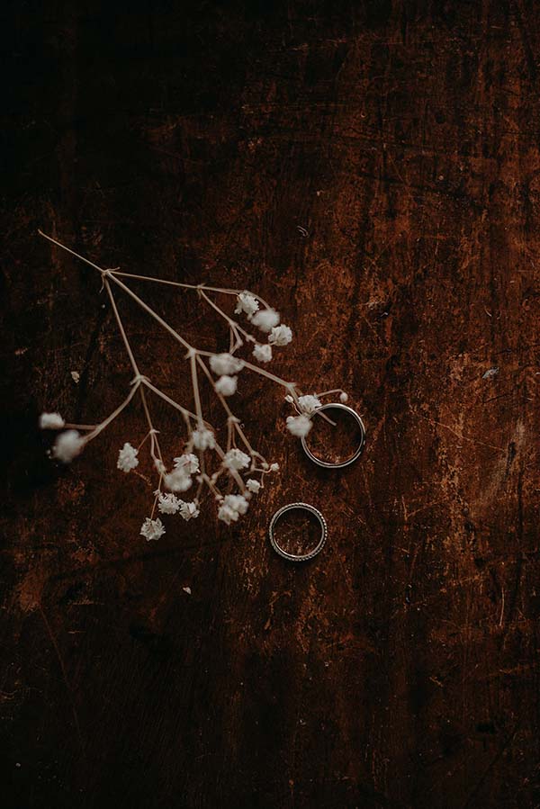 Deux alliances en argent et un brin de gypsophile blanc sur un fond de bois sombre et rustique.
