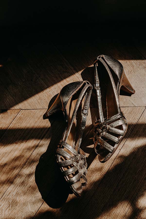 Paire de sandales à talons dorées et scintillantes posée sur un parquet en bois, éclairée par une lumière naturelle.
