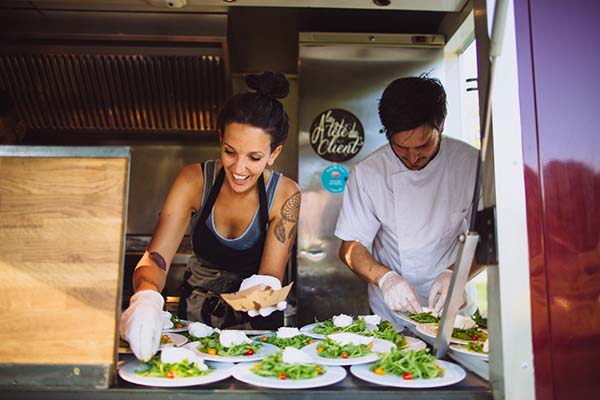 Deux chefs souriants préparent des assiettes colorées dans un food truck lors d'un mariage bucolique.
