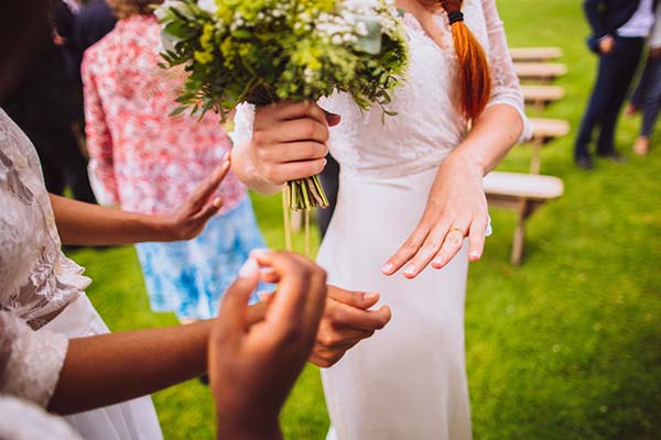 Gros plan d'une mariée en robe blanche tenant un bouquet champêtre lors d'une cérémonie en plein air.