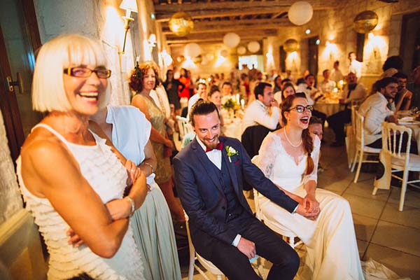 Invités souriants et mariés élégants lors d'une réception chaleureuse dans une salle aux tons crème et bois.