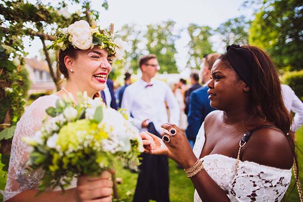 Une mariée couronnée de fleurs rit aux éclats avec une invitée lors d'un mariage bucolique en plein air.