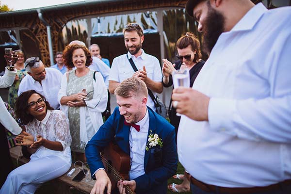 Un musicien à la guitare divertit des invités souriants et élégants lors d'un cocktail de mariage en plein air.