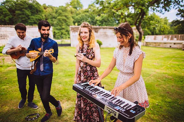 Quatuor de musiciens joyeux jouant du clavier et des guitares dans un jardin verdoyant et lumineux.