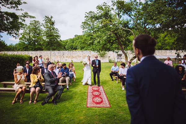 Cérémonie de mariage en plein air avec tapis rouge, invités élégants et décor champêtre verdoyant.