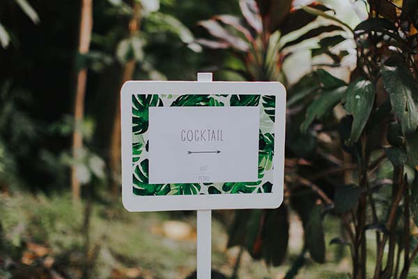 Panneau blanc indiquant Cocktail avec un cadre de feuilles tropicales vertes dans un jardin luxuriant.