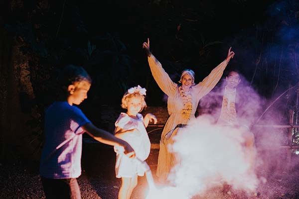 Une famille joyeuse célèbre un événement nocturne à Bali entourée de fumée colorée et de lumières chaleureuses.