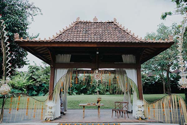 Pavillon balinais traditionnel décoré de voilages blancs et de fleurs pour une cérémonie de mariage en plein air.