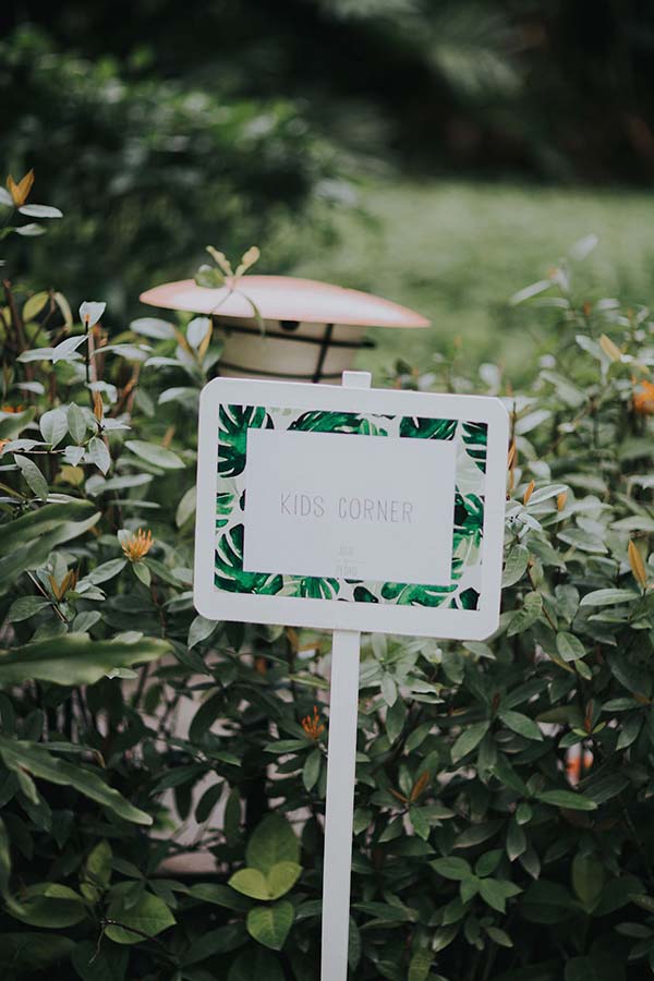 Panneau blanc avec l'inscription Kids Corner entouré de feuilles tropicales vertes dans un jardin luxuriant.