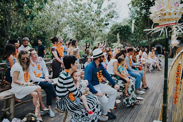 Invités élégants portant des colliers de fleurs orange lors d'une cérémonie en plein air à Bali.