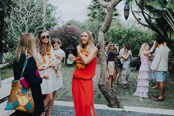 Invités souriants portant des colliers de fleurs orange lors d'une cérémonie festive en extérieur à Bali.