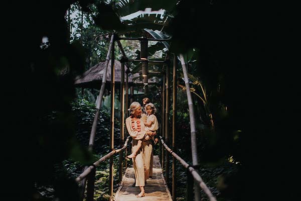 Couple en tenues blanches s'enlaçant sur un pont en bois dans un jardin tropical luxuriant à Bali.