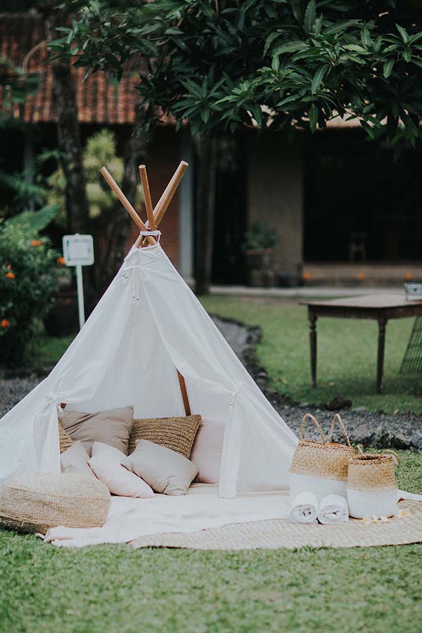 Tente tipi blanche avec coussins et paniers en osier sur une pelouse verdoyante, ambiance bohème et relaxante à Bali.