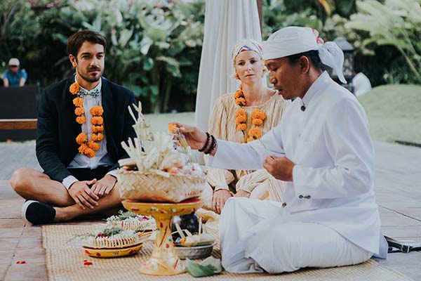 Couple en tenue de cérémonie et prêtre balinais lors d'un rituel traditionnel avec des offrandes colorées à Bali.