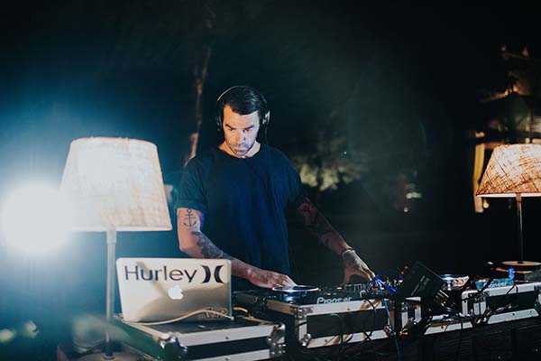 Un DJ mixant derrière ses platines dans une ambiance nocturne tamisée et élégante.