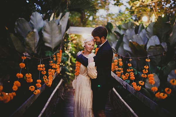 Couple s'enlaçant tendrement dans un jardin tropical balinais, entouré de fleurs orange et de feuillages luxuriants.