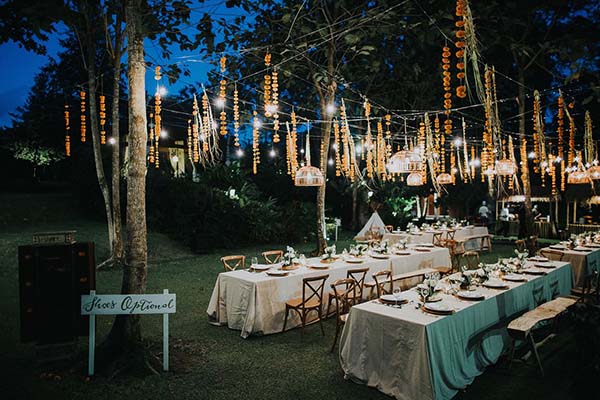 Dîner en plein air à Bali avec tables dressées et guirlandes lumineuses sous un ciel bleu crépusculaire.