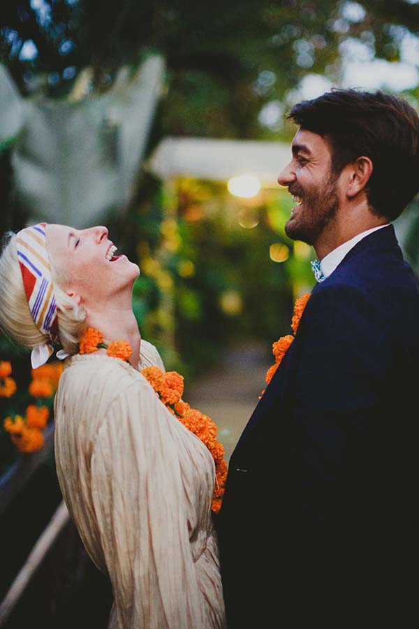Couple riant avec des colliers de fleurs orange lors d'un renouvellement de vœux à Bali.