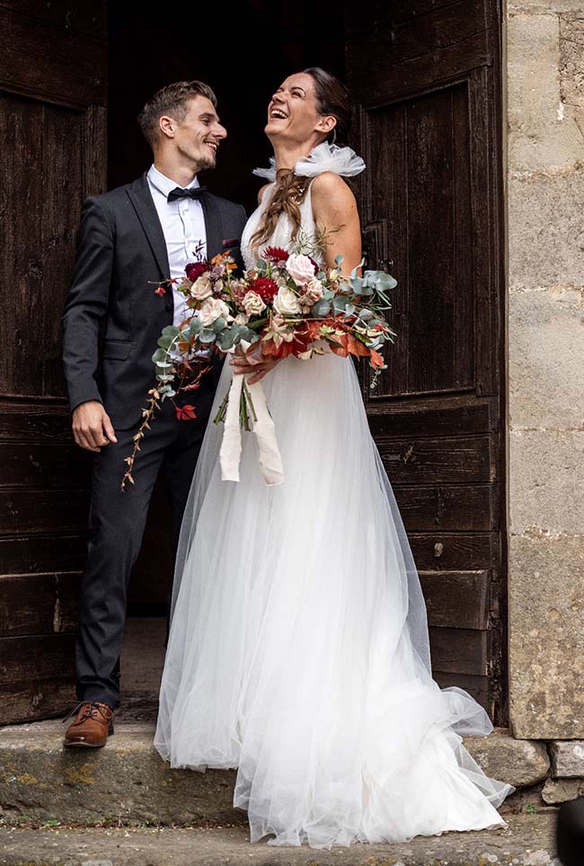 Un couple heureux debout sur des marches, le mari en costume noir et le mariée dans un robe blanche floue, tenant un