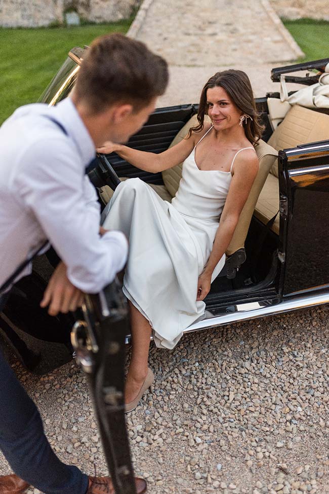 Une jeune femme en robe blanche élégante monte dans un limousine, souriant, pour un mariage simple et élégant.