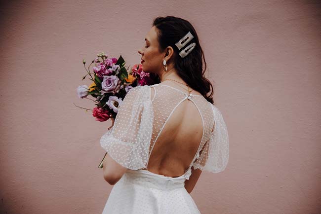 Élégante mariée tenant un bouquet coloré contre un fond rose, incarnant la beauté romantique d'un elopement à la française.