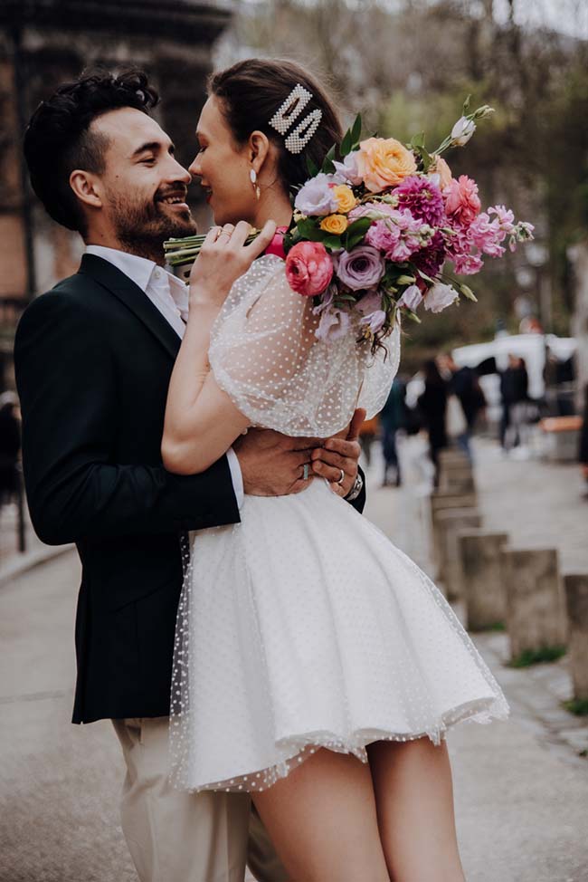 Un couple éblouissant dans des vêtements de mariage romantiques, partageant un moment tendre contre un décor urbain charmant.