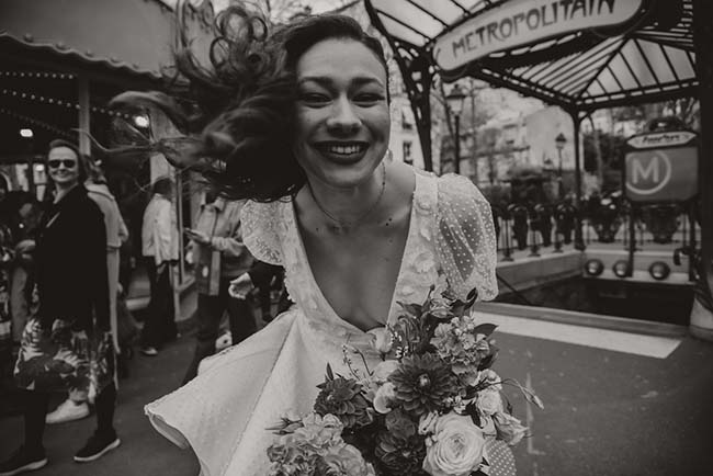 Une jeune mariée se balancant dans la rue parisienne, son bouquet de fleurs en relief contre un décor noir et blanc.