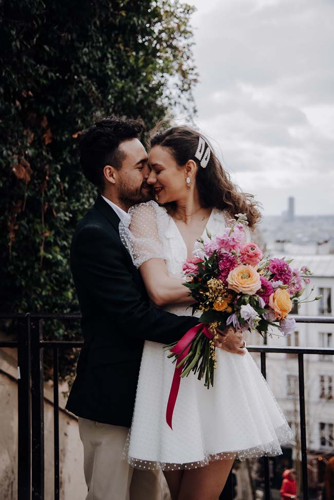 Un couple charmant se baigne dans l'émotion sur une terrasse avec une bouquet coloré, incarnant l'élégance et la joie du mariage.