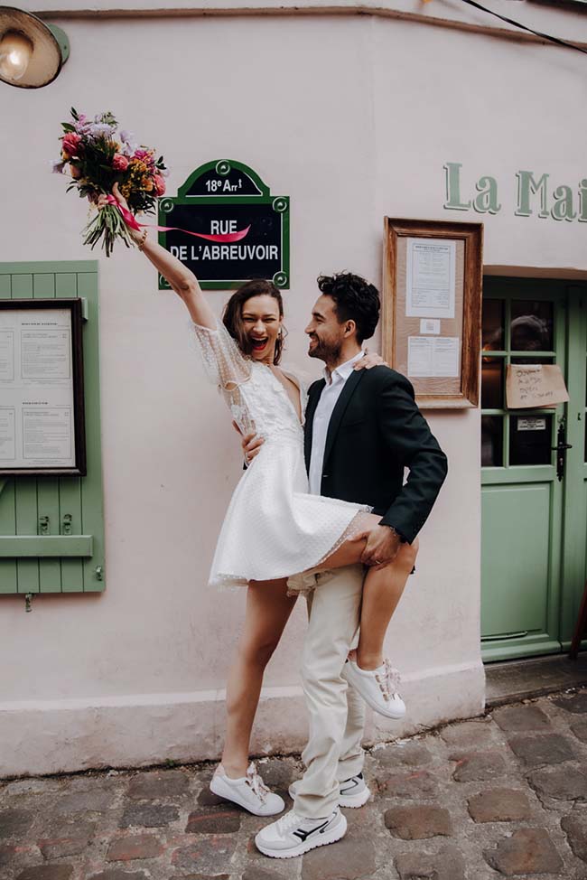 Joyeux couple dans une rue de Paris romantique, célébrant leur elopement avec des sourires exaltés et des fleurs colorées.