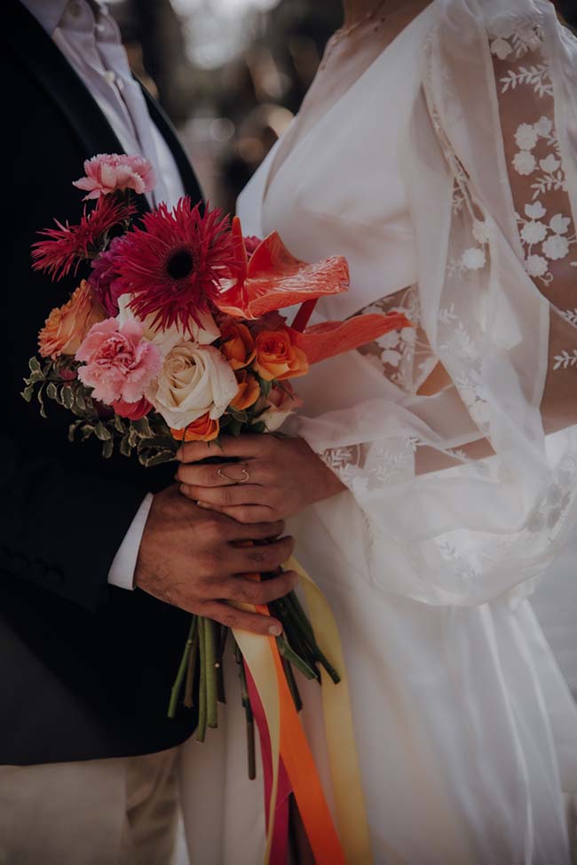 Un bouquet de fleurs colorés dans la main d'une mariée, décorant l'ambiance romantique d'un elopement à la française.