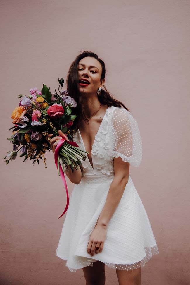 Une mariée joyeuse dans une robe blanche légère, tenant un bouquet coloré de roses, incarnant l'élégance et la joie