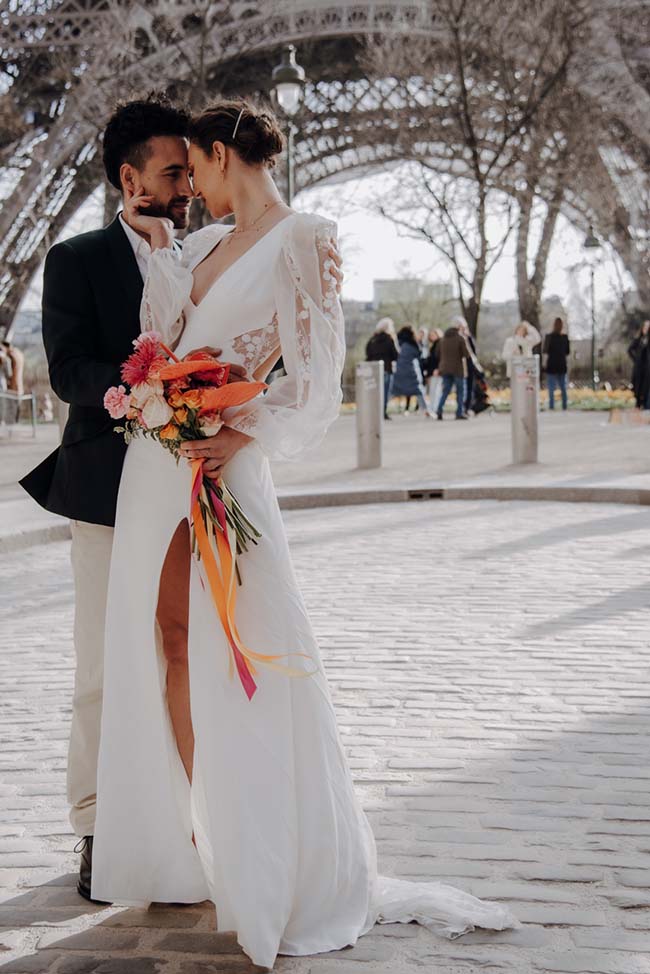 Une nouvelle mariée dans un vêtement blanc élégant et raffiné, tenant un bouquet coloré, se détache contre le décor