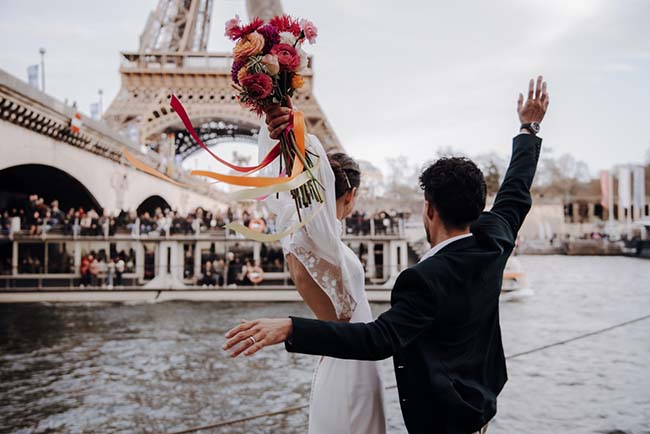 Un couple enthousiaste célèbre leur mariage à l'extérieur du pont de l'Europe, avec un bouquet coloré en coulisse.