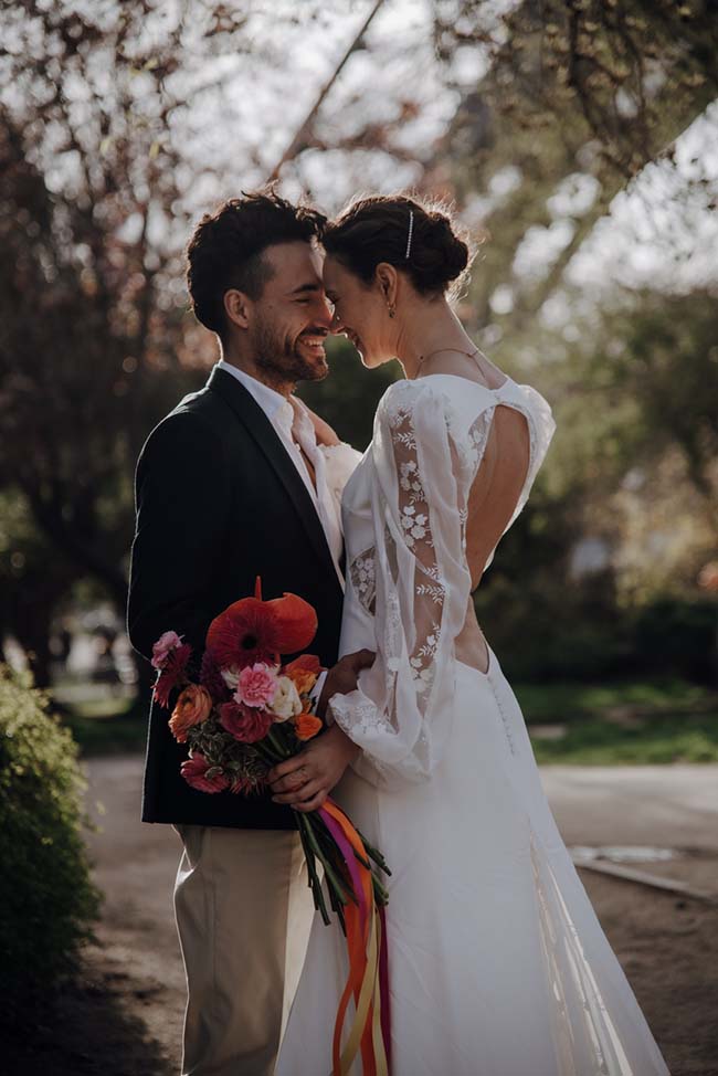 Un couple heureux se tient dans un parc, le mari tenant un bouquet coloré et le mariée tenant une robe blanche