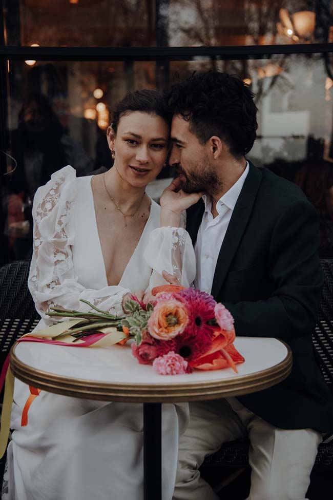 Un couple émerveillé partage un moment intime au sein d'un décor romantique, avec des fleurs colorées et un ambiance chaude.