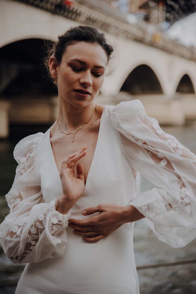 Élégante mariée en robe blanche avec manches en guimauve, posant devant un pont romantique.