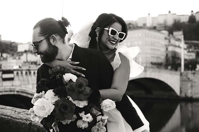 Une mariée exaltée dans un robe noire et blanche tient un bouquet de roses et d'orchidées, embrassant son mari qui