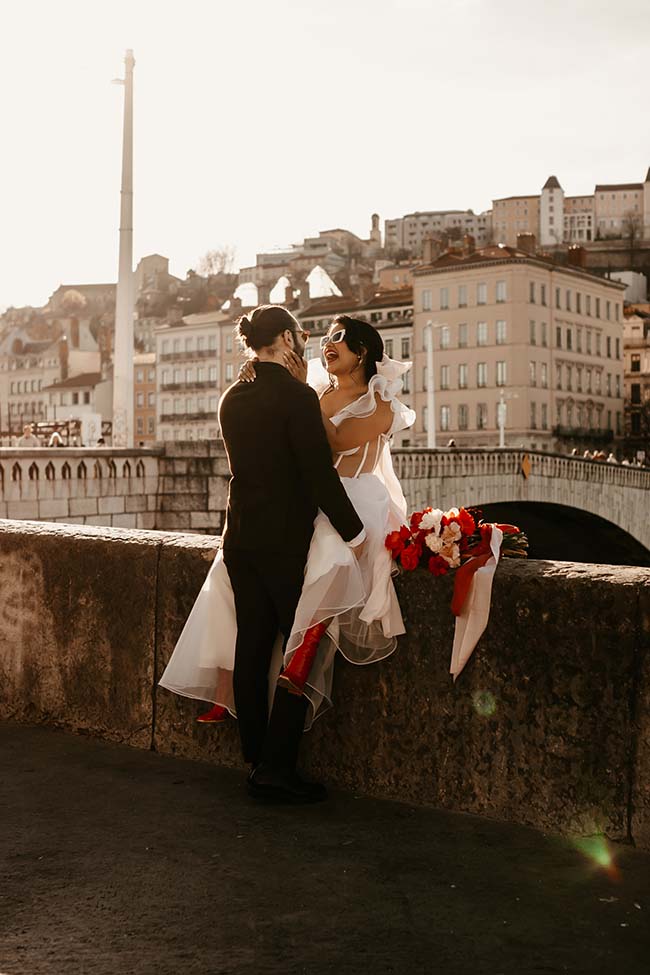 Un couple de mariés exaltés en amour contre un décor urbain charmant, avec des tons chauds et romantiques.