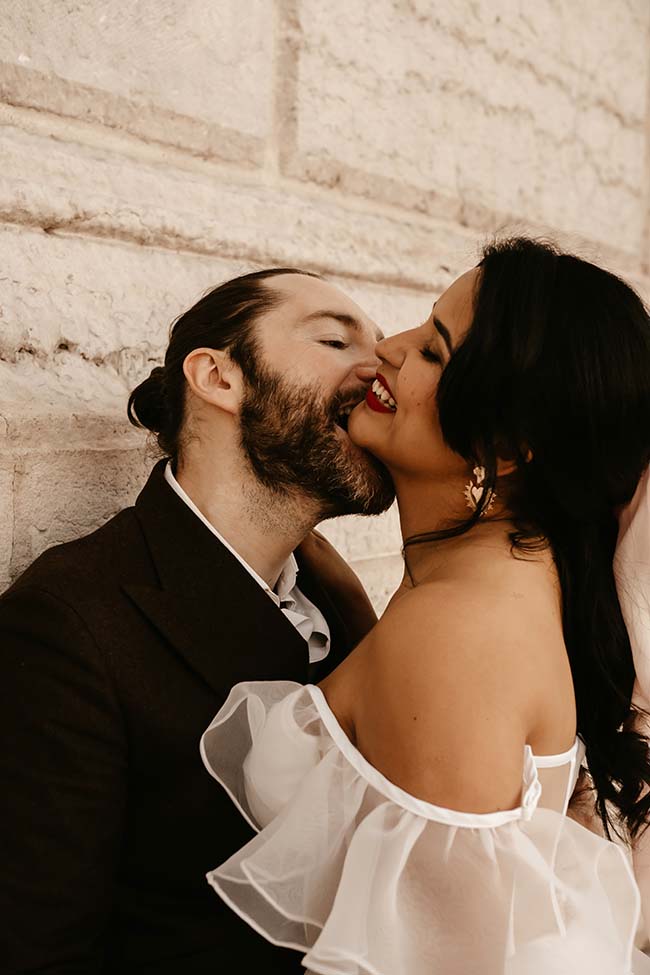 Un couple heureux dans des vêtements de mariage sombre et éclatant, échangeant des caresses tendres contre un mur en