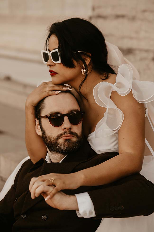 Un couple romantique en mariée et costume noir, partageant un moment intime dans un décor urbain chaud et accueillant.