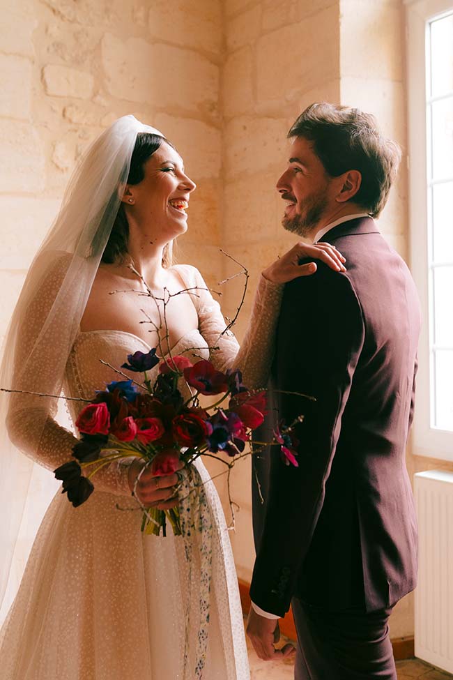 Une mariée heureuse dans sa robe blanche, tenant un bouquet de fleurs vives, se trouve dans un décor romantique avec son mari.